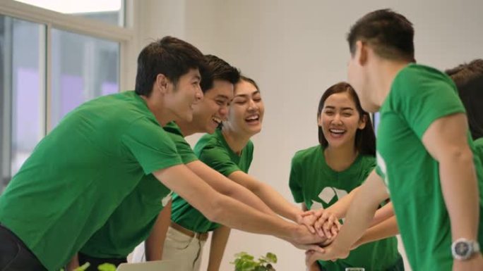 4k志愿者团队开会。一群穿着绿色t恤的亚洲年轻人志愿者在现代办公室里团结一致，团队合作。