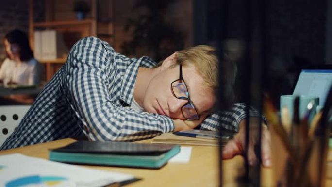 在黑暗的办公室里睡在桌子上的帅哥的慢动作在工作中放松