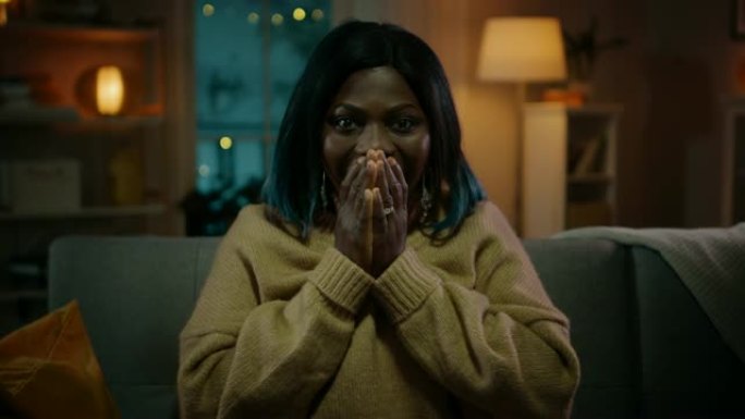 一个美丽的黑人女孩的肖像晚上坐在家里的沙发上，在电视上看恐怖电影。她真的很害怕和情绪化。