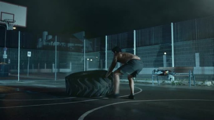 强壮的肌肉健康的年轻光着膀子的男人正在一个有围栏的室外篮球场里做运动。在一个居民区雨后的雾蒙蒙的夜晚