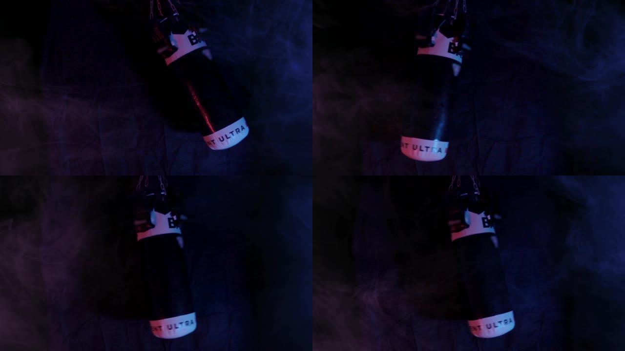拳击袋在现代紫外线蓝紫色荧光色的黑暗背景下在烟雾中摇摆