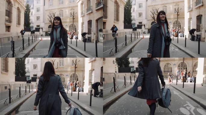 快乐美丽的旅行者女人，带着相机为相机摆姿势，沿着秋天的巴黎街道微笑慢动作行走。