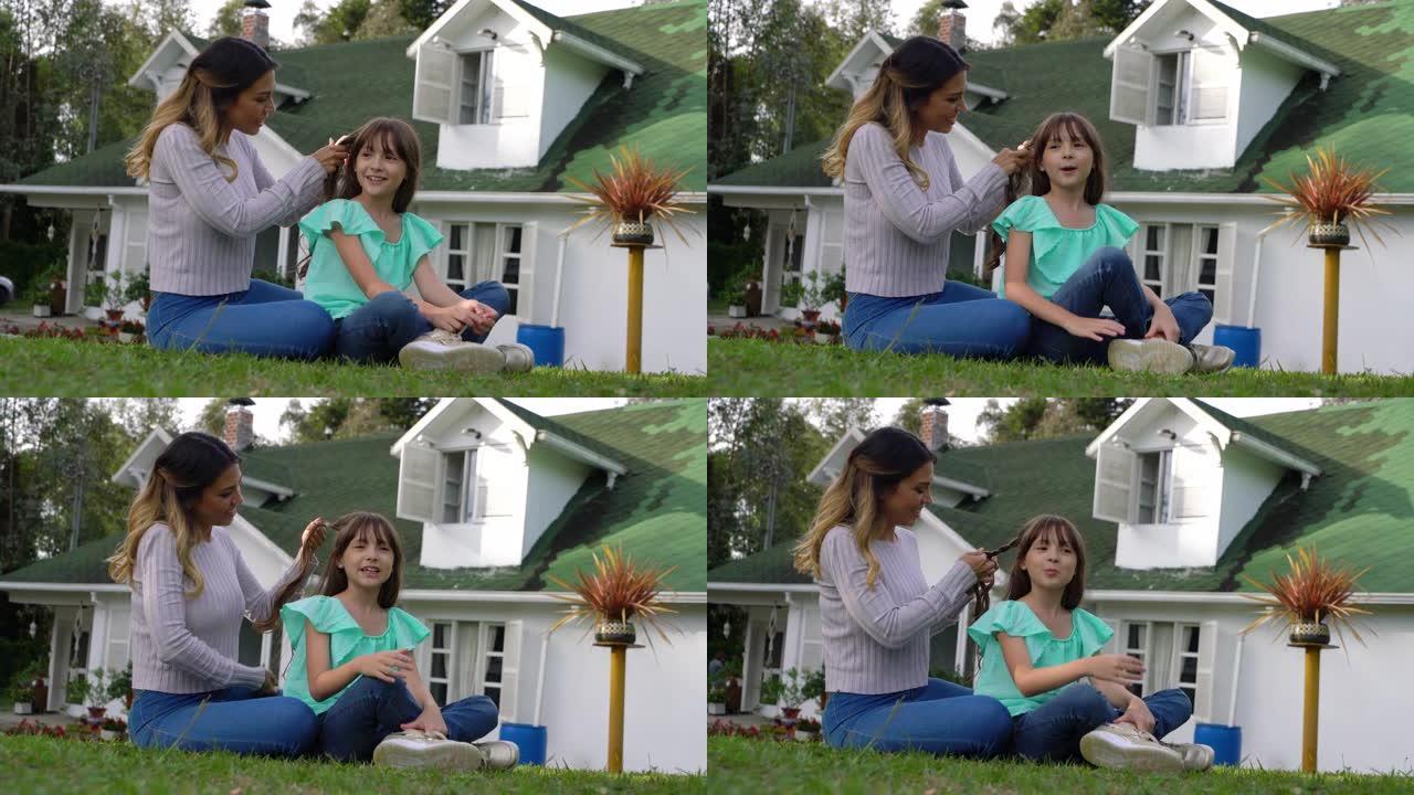 慈爱的母亲坐在后院聊天和微笑时给女儿做辫子