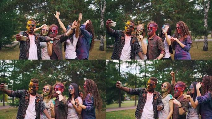 快乐的年轻人戴着墨镜的慢动作，脸上有肮脏的脸和头发跳舞，在派对上自拍时在智能手机上笑着录制视频。