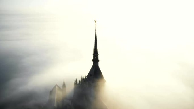 无人驾驶飞机在诺曼底阳光云层上方圣米歇尔山城堡尖顶雄伟的金色雕像上方飞行。