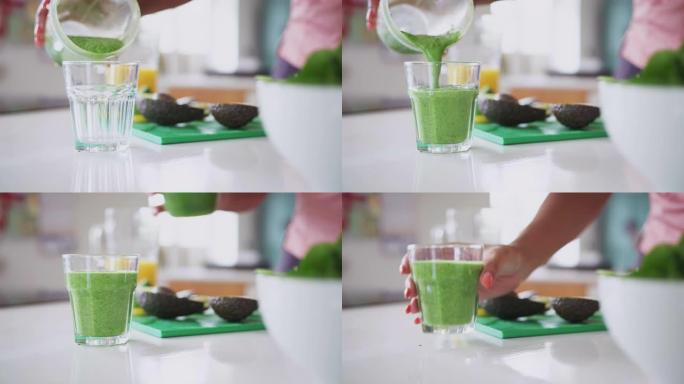 女人将健康的果汁饮料从搅拌机倒入玻璃杯中的特写镜头