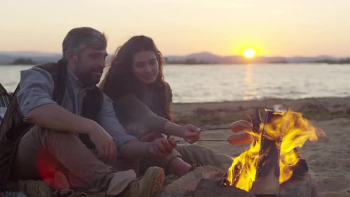 夫妻在日落时在海滩上的火上煮香肠