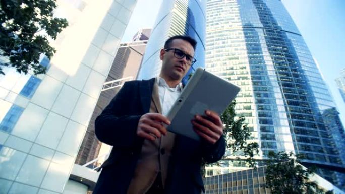 男商人，经理正站在摩天大楼附近，用平板电脑。