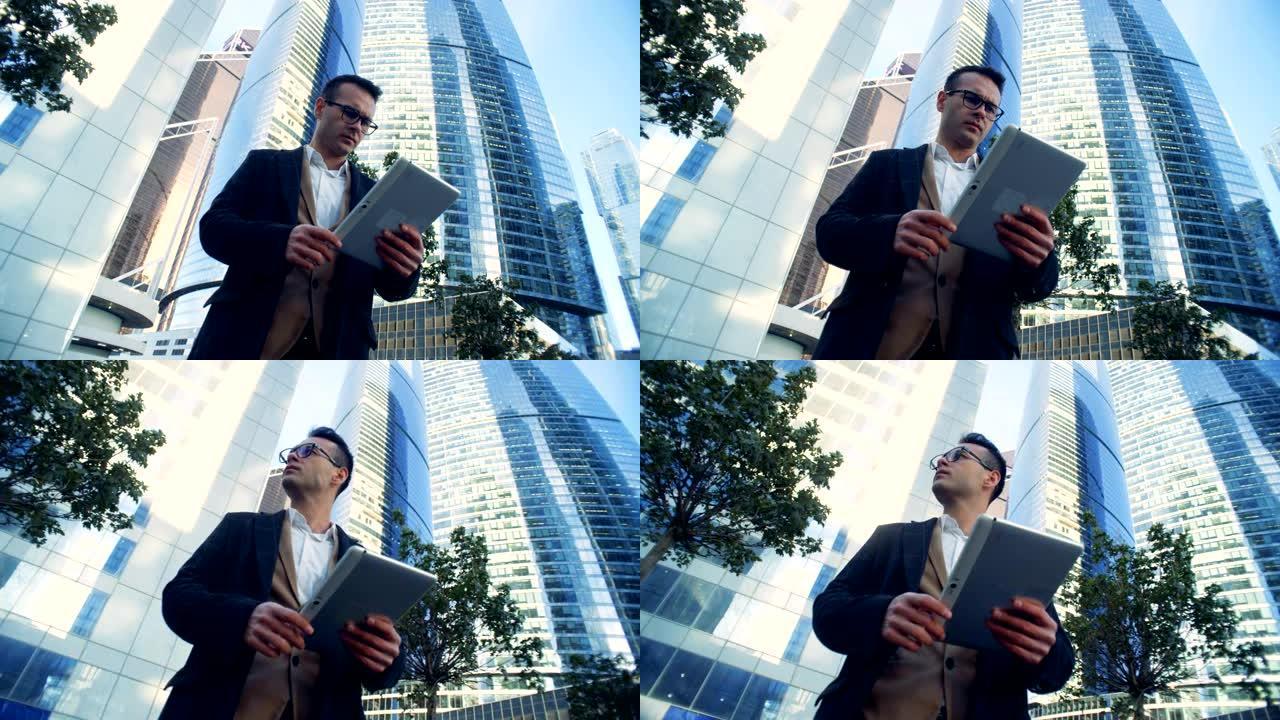 男商人，经理正站在摩天大楼附近，用平板电脑。