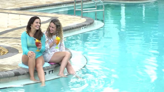 西班牙裔姐妹在游泳池旁喝热带饮料