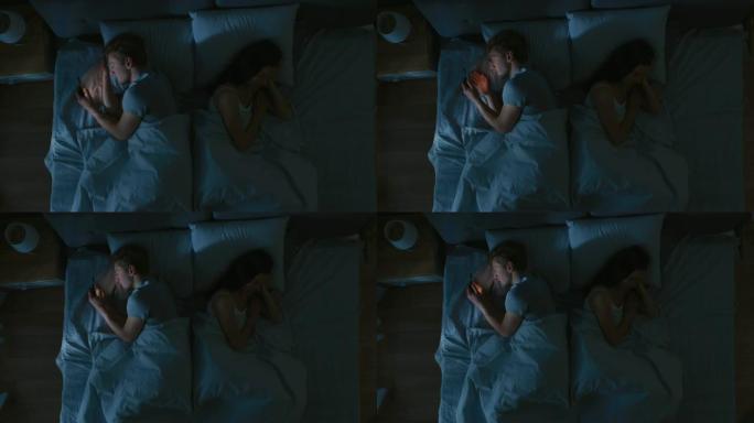 失眠症压力大的年轻人晚上在床上睡觉时用智能手机，女朋友睡得很甜很香。顶视图摄像机