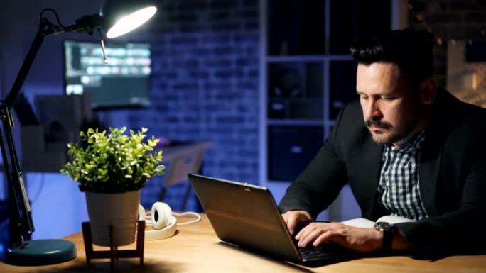 男性员工使用笔记本电脑晚上在办公室加班忙于项目