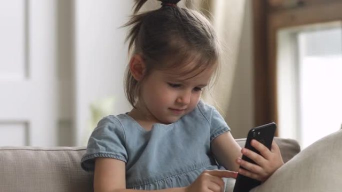 可爱的聪明的小女孩独自在家使用智能手机