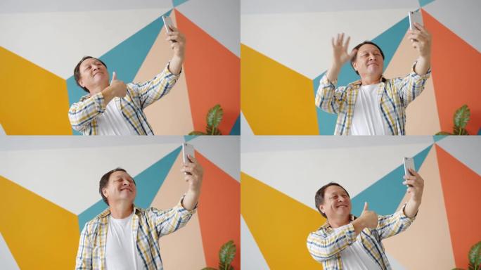 快乐的亚洲男子在家中用智能手机相机自拍，展示手势