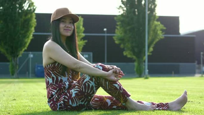 年轻的亚洲妇女坐在休闲服装的草地上