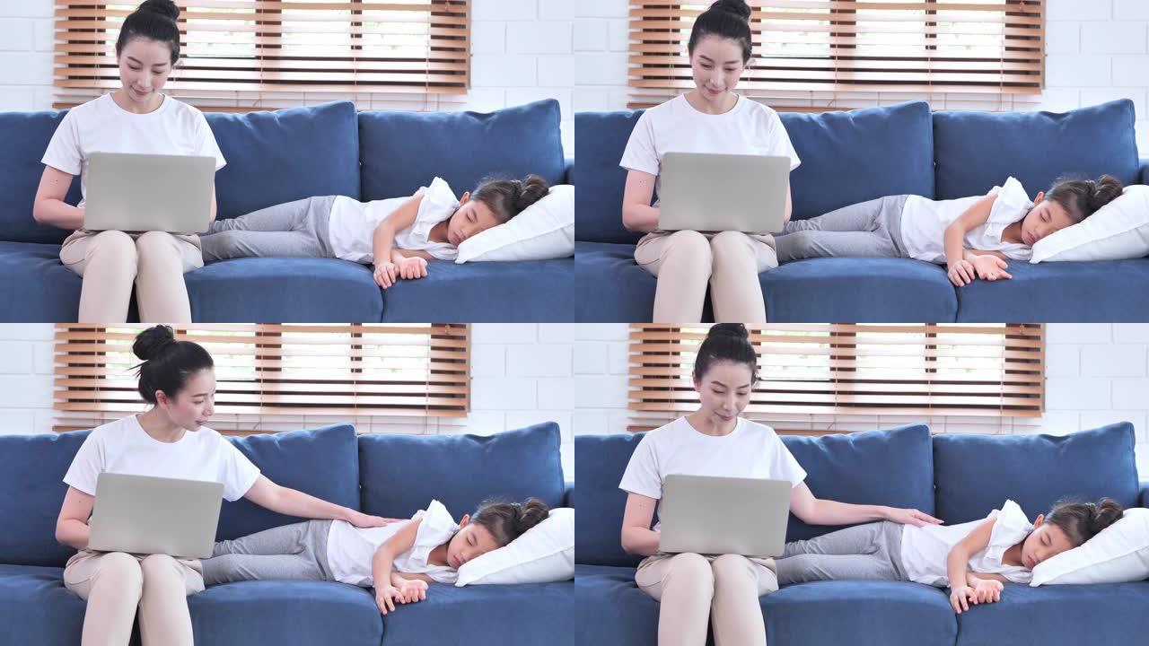 亚洲母亲在社交距离中使用笔记本电脑在家里工作，以防止新冠病毒或Covid-19的流行，同时她触摸睡在