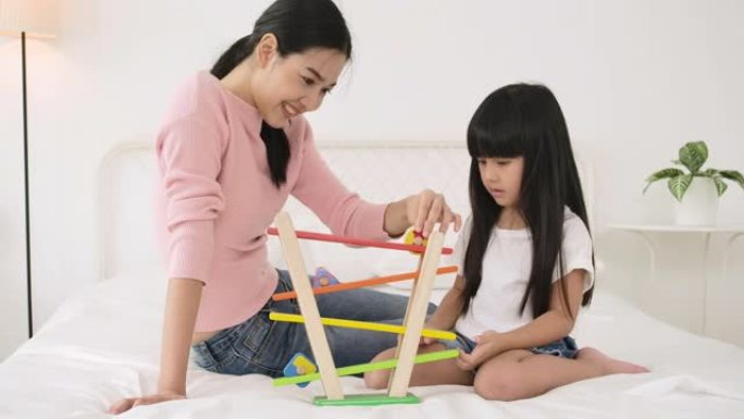 幸福的家庭年轻妈妈保姆和可爱的小女儿一起玩彩色木头玩具。