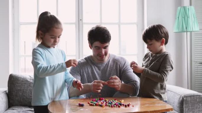 快乐的年轻父亲帮助孩子们一起制作手工项链