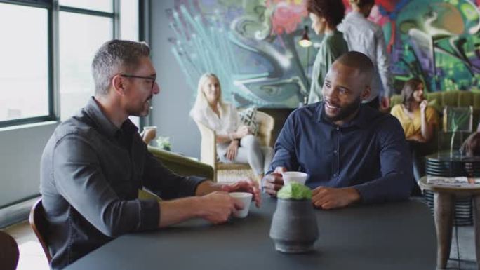 两名男性创意同事在他们的工作场所咖啡馆里聊天，四分之三长，弧拍