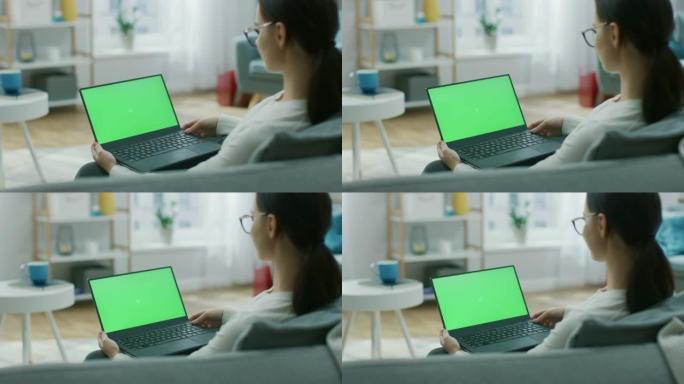 坐在沙发上的年轻女子在带有绿色模拟屏幕的笔记本电脑上工作。女孩使用电脑，浏览互联网，观看内容，与朋友