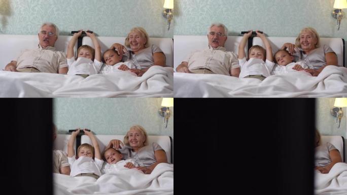 孩子们躺在床上和祖父母一起看电视
