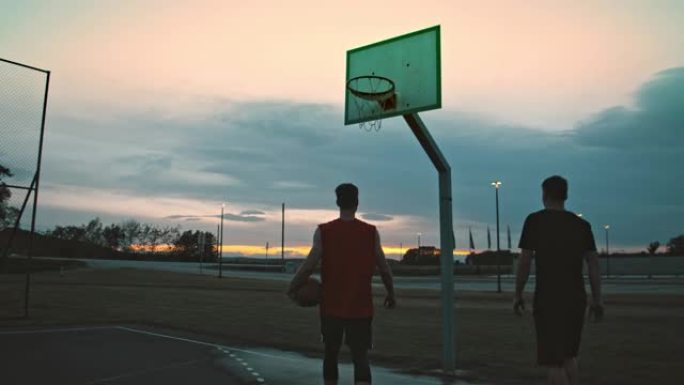 年轻男子女士在黄昏时走出室外篮球场。两个朋友离开户外篮球。
