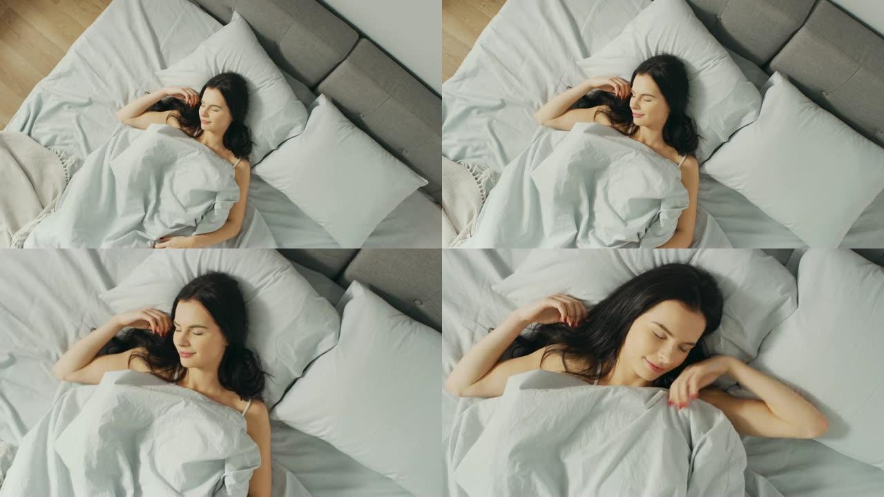 美丽的年轻黑发女人在清晨迷人地睡在她的床上。安静睡觉的女孩甜美温暖的景色。自上而下放大相机拍摄。