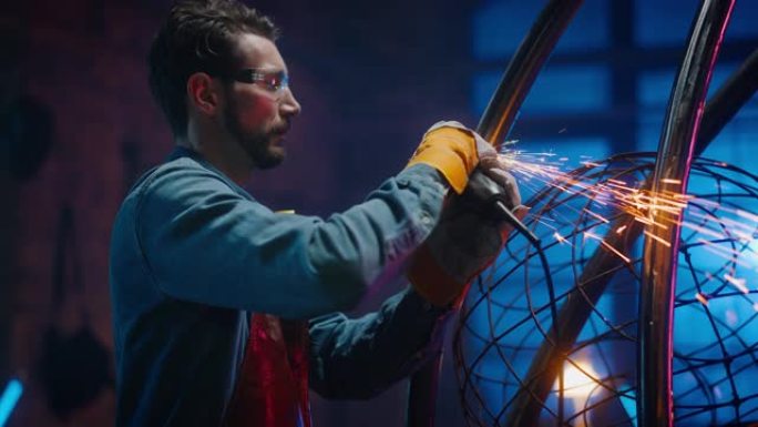 年轻的当代艺术家正在工作室里用手持电动工具打磨他的金属管雕塑。专业人士用金属制作现代残酷的抽象艺术品