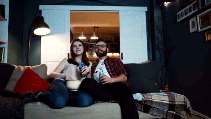 快乐的年轻高加索浪漫学生夫妇在家里用投影仪慢动作一起看电影。