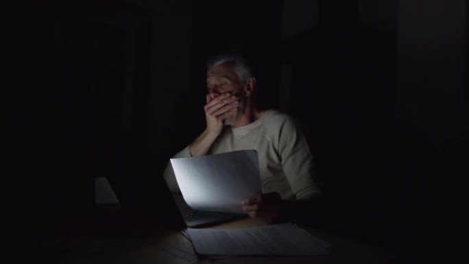 疲倦的高加索人深夜工作，看着笔记本电脑和文件