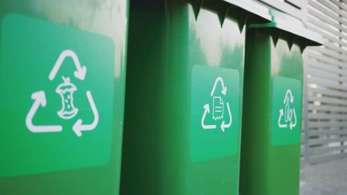 绿色的塑料垃圾桶，前面有不同的回收标志，靠着棕色的木墙排成一排。食品、纸张和瓶子的废物分类概念。从垃