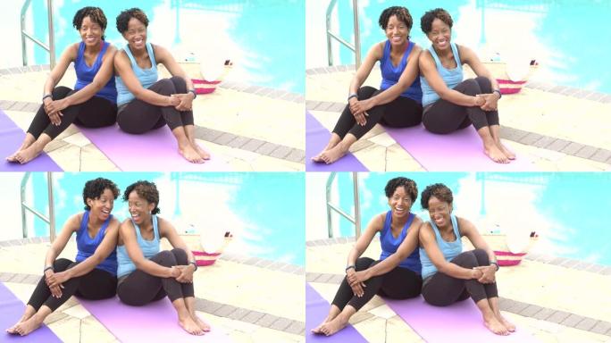 同卵双胞胎姐妹坐在游泳池旁的运动垫上