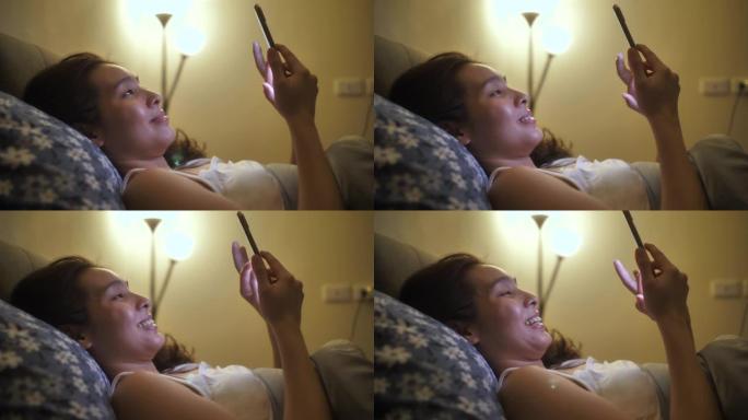 亚洲女人使用智能手机晚上在床上微笑快乐