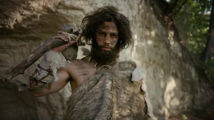 原始穴居人的肖像戴着动物皮，手持石尖锤。史前尼安德特人猎人在丛林中与原始狩猎合影。看着相机
