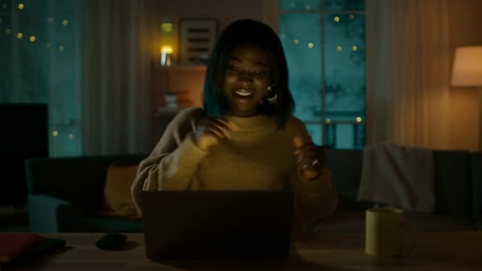 晚上: 快乐美丽的女孩坐在办公桌前跳舞，她用笔记本电脑听音乐。
