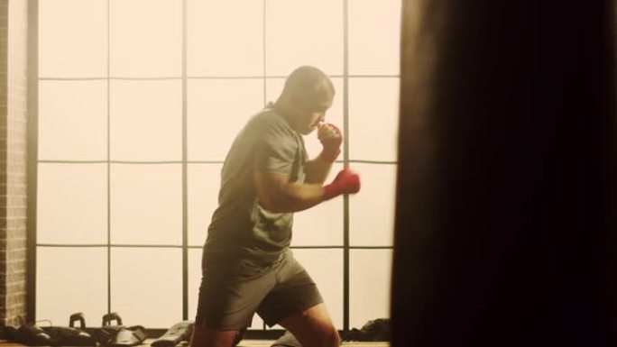 强壮英俊的男拳击手正在一个大窗户的阁楼健身房锻炼。男性运动员正在空中练习拳击。他很认真，精力充沛。房