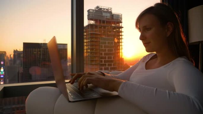 特写: 当金色的阳光照进她的房间时，年轻女子在笔记本电脑上工作