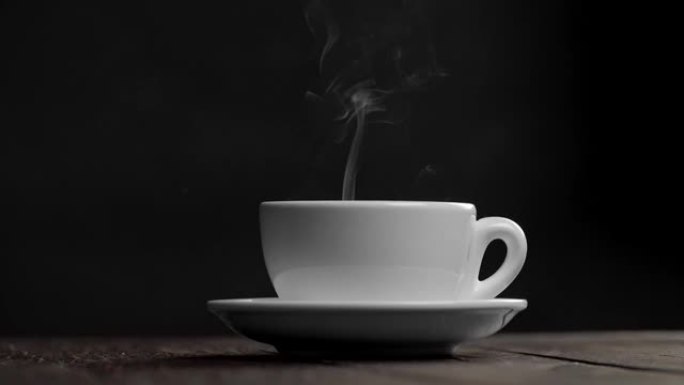 在黑色背景下的碟子上热的白茶或咖啡杯。杯子里冒出蒸汽或烟雾。慢动作镜头