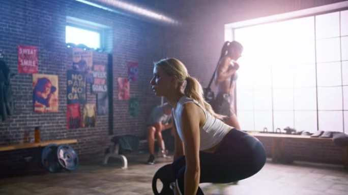 美丽健康的运动金发女性从地面上举起杠铃，做背部强化锻炼，作为她日常的健身训练程序。她在阁楼健身房和运