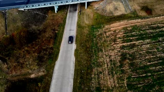 空中俯视图，摄像机跟踪在大气公路旅行中沿着侵蚀的田野和高速公路行驶的黑色汽车。