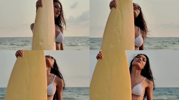 美丽性感的年轻女子穿着比基尼冲浪女孩，日落或日出时在海滩上冲浪板。日落时穿着性感比基尼的辣妹。假期-