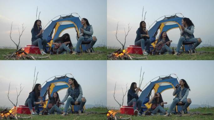 慢动作-一群年轻的亚洲女孩在湖边露营，弹吉他，在帐篷前一起唱歌。露营、旅行和友谊概念。