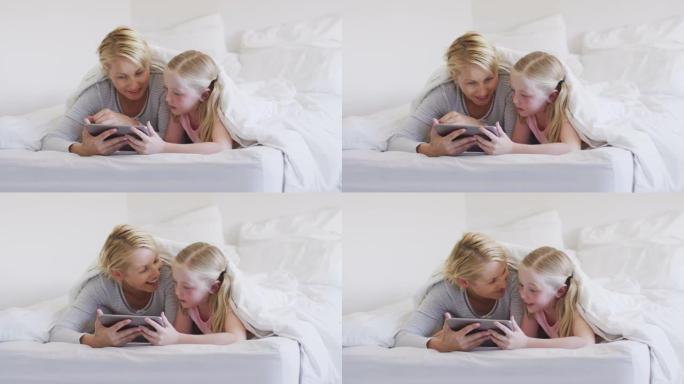 白人妇女和她的女儿在床上使用数字平板电脑的前视图
