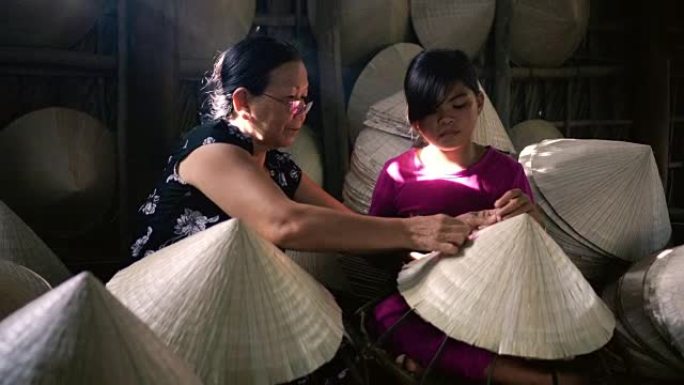 4k镜头越南老工匠教孙子在越南坎托省Ap Thoi Phuoc村的老传统房子里制作传统越南帽子的弱光