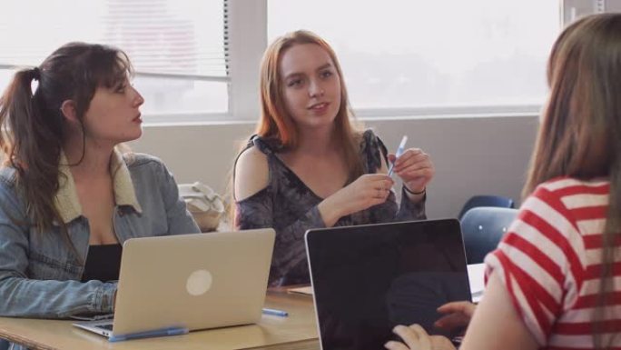 一群使用笔记本电脑坐在办公桌前的女大学生共同参与项目