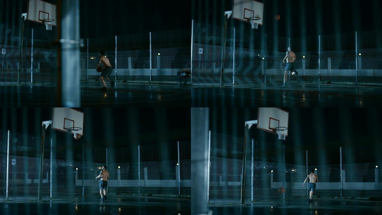 运动年轻的男子篮球运动员运球并在围栏的街球场上扔球。进了一个两分球。居民区雨后的夜间录像。