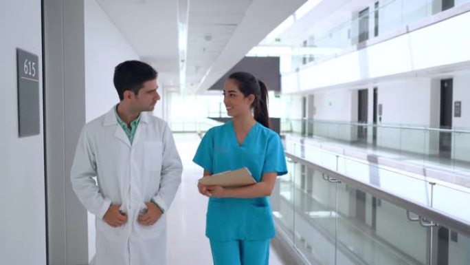 医生拿着剪贴板听护士讲话，并讨论在医院走廊上行走的病例