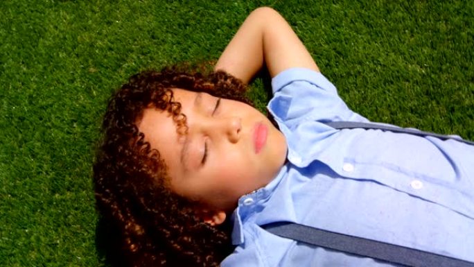 在阳光4k的学校操场上，混血女学生在草地上放松的高角度视角