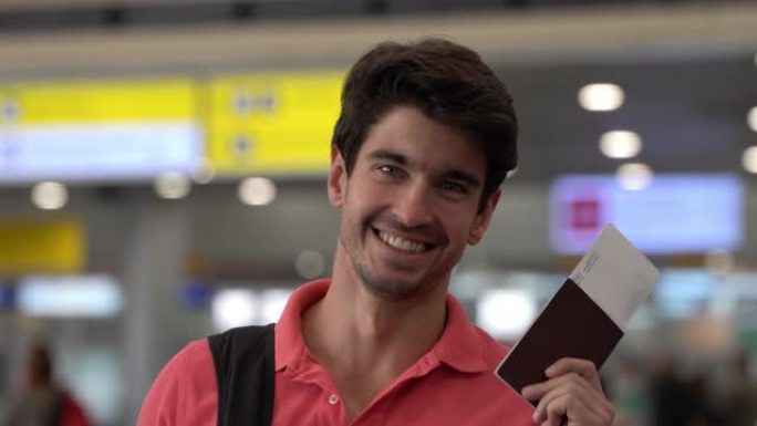 高加索英俊男子拿着护照和登机牌在机场准备旅行，面对镜头微笑