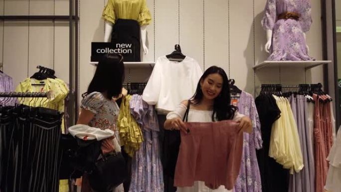 2位年轻的亚洲华裔女性朋友在购物中心的精品店购物，选择新衣服